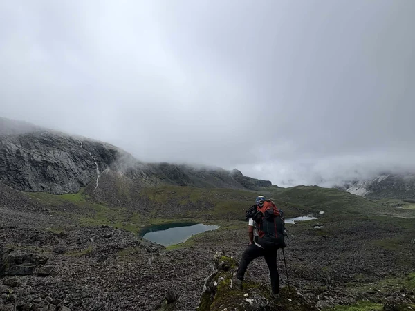 Trekker on rocky ground above a small alpine lake