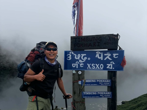 Smiling trekker beside the Timbung Pokhari signboard in mist
